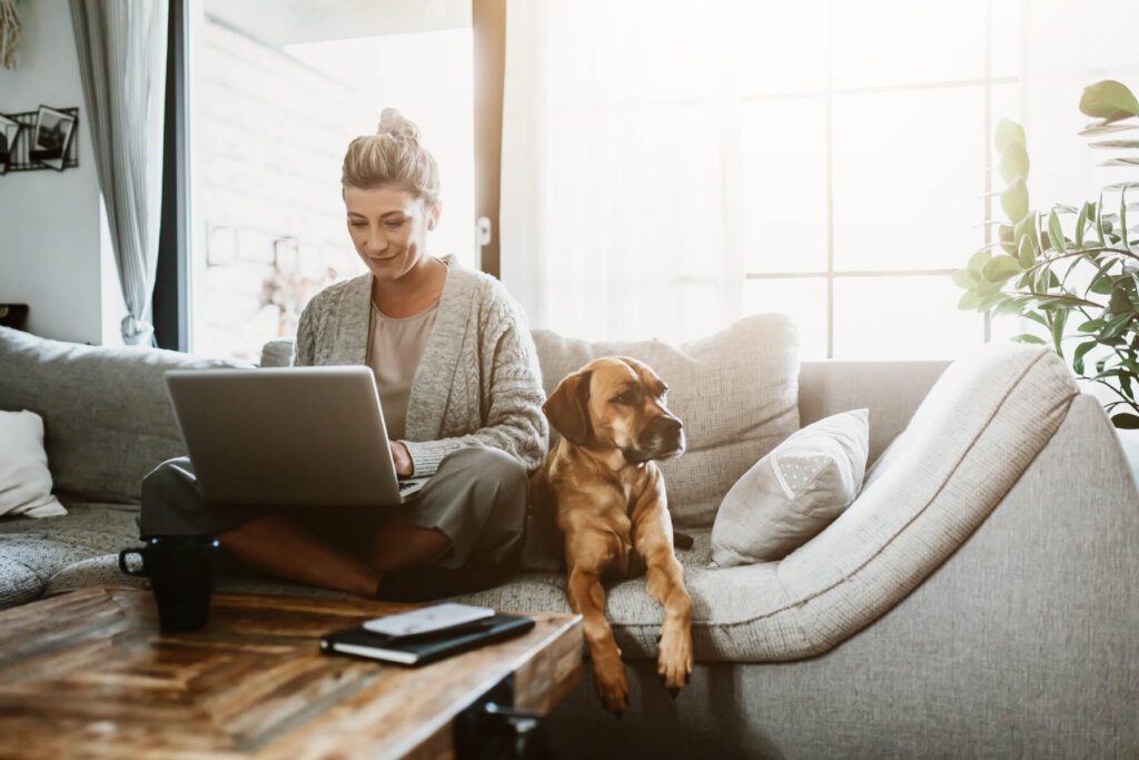 Dog On Couch Next To Owner With Laptop On Lap